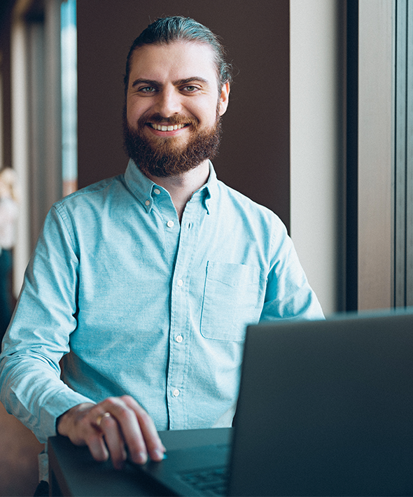 En mand står foran sin computer og smiler til kameraet